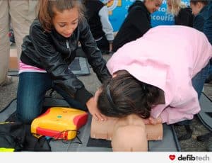 enfants pratiquant le massage cardiaque sur un mannequin de formation avec un DAE
