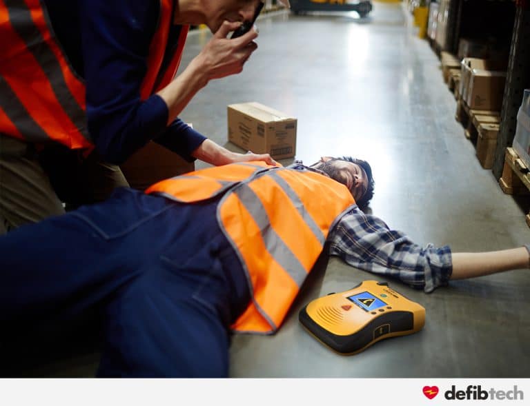 Secouriste appelant les secours et prêt à intervenir avec le défibrillateur lifeline view sur une victime d'acr dans un entrepôt