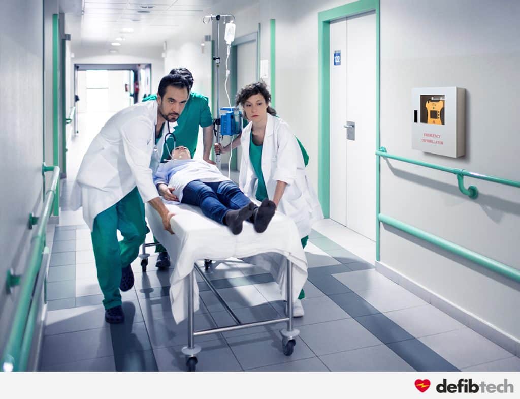 Médecins et infirmiers conduisant un brancard dans un couloir d'hôpital avec un défibrillateur accroché au mur dans un boitier